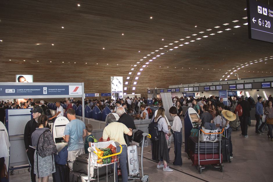 Travellers queuing with luggage trolleys among the check-in desks in the departures hall at Paris Charles de Gaulle airport.